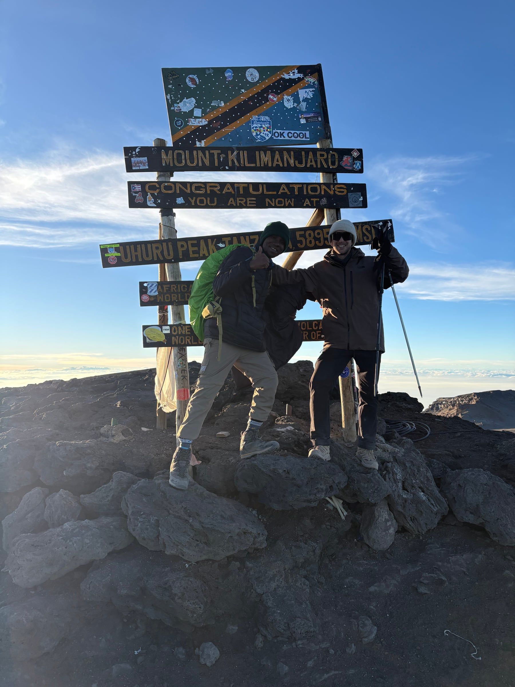 A guide and a climber celebrate at sunrise in front of the Uhuru Peak sign on Kilimanjaro's summit, 5,895 m